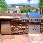 Beige stone and paver BBQ set up on patio with green bushes and trees in background