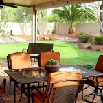 Metal patio furniture with orange cushions on brick floor in front of grass and tree landscaped yard